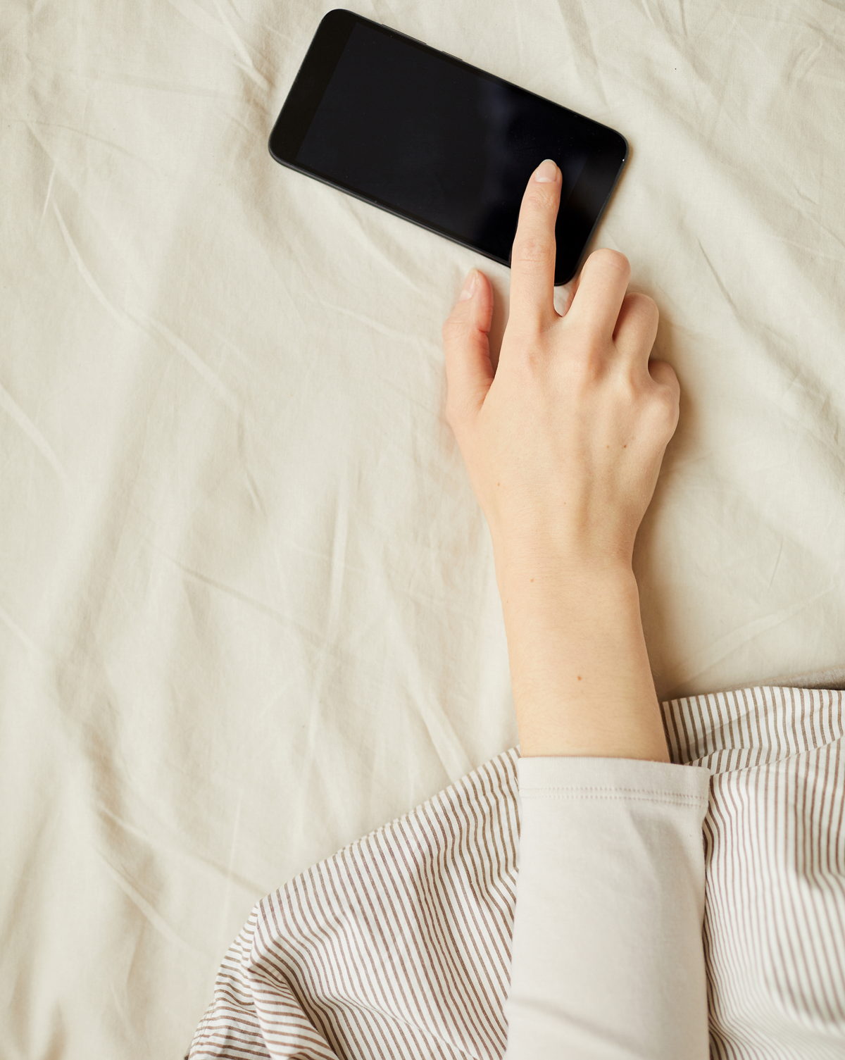 Hand turning off a smartphone on the bed to switch to Do Not Disturb before sleep