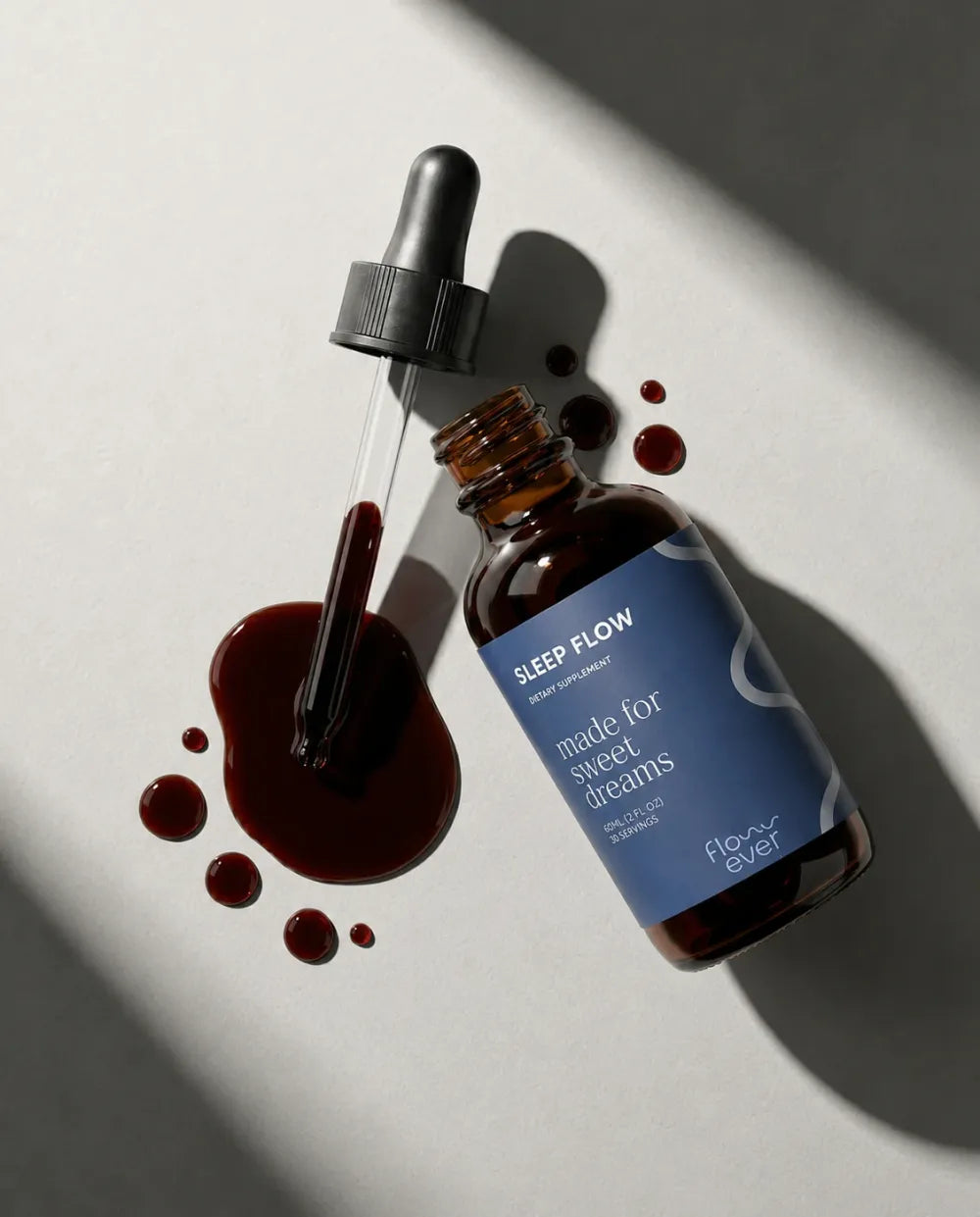 Sleep Flow bottle lying beside its dropper and a few drops of the dark red liquid